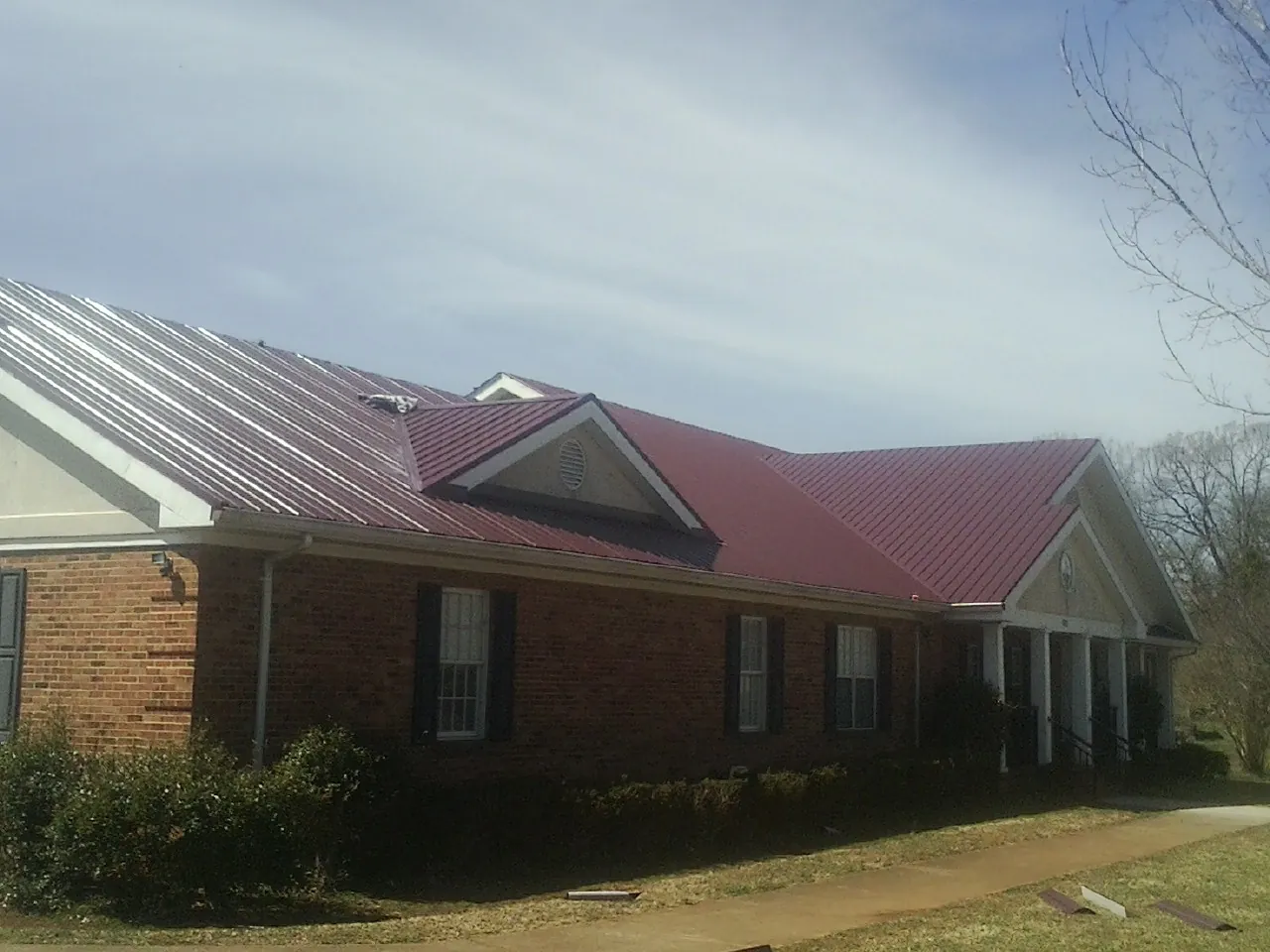 Red metal roof with gabled entries on a long brick building, from a Hail Damage Roof Repair job in Fort Walton Beach