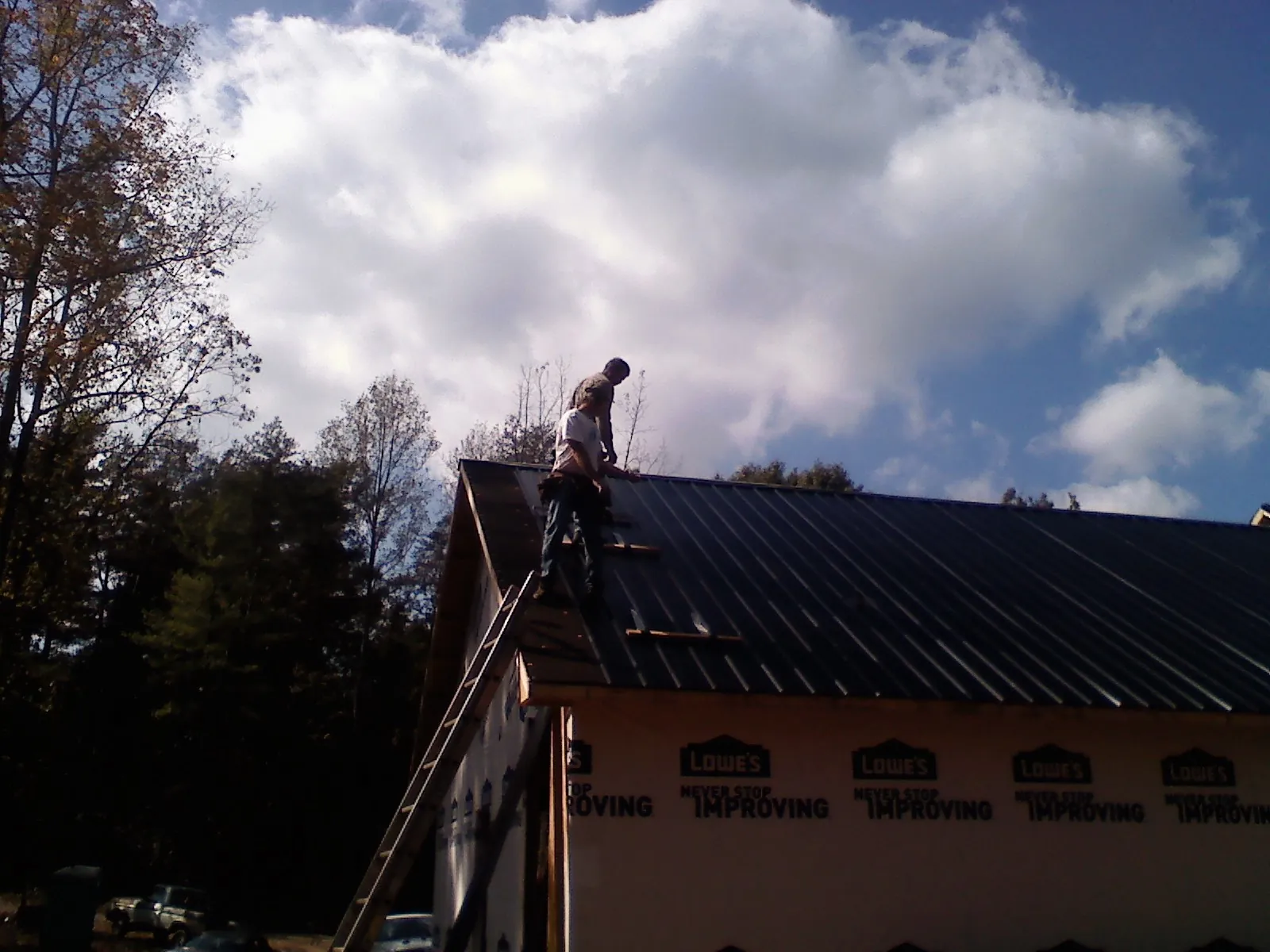 Roofer fastening dark metal panels high against a cloudy sky, from a Roof Inspection job in Fort Walton Beach
