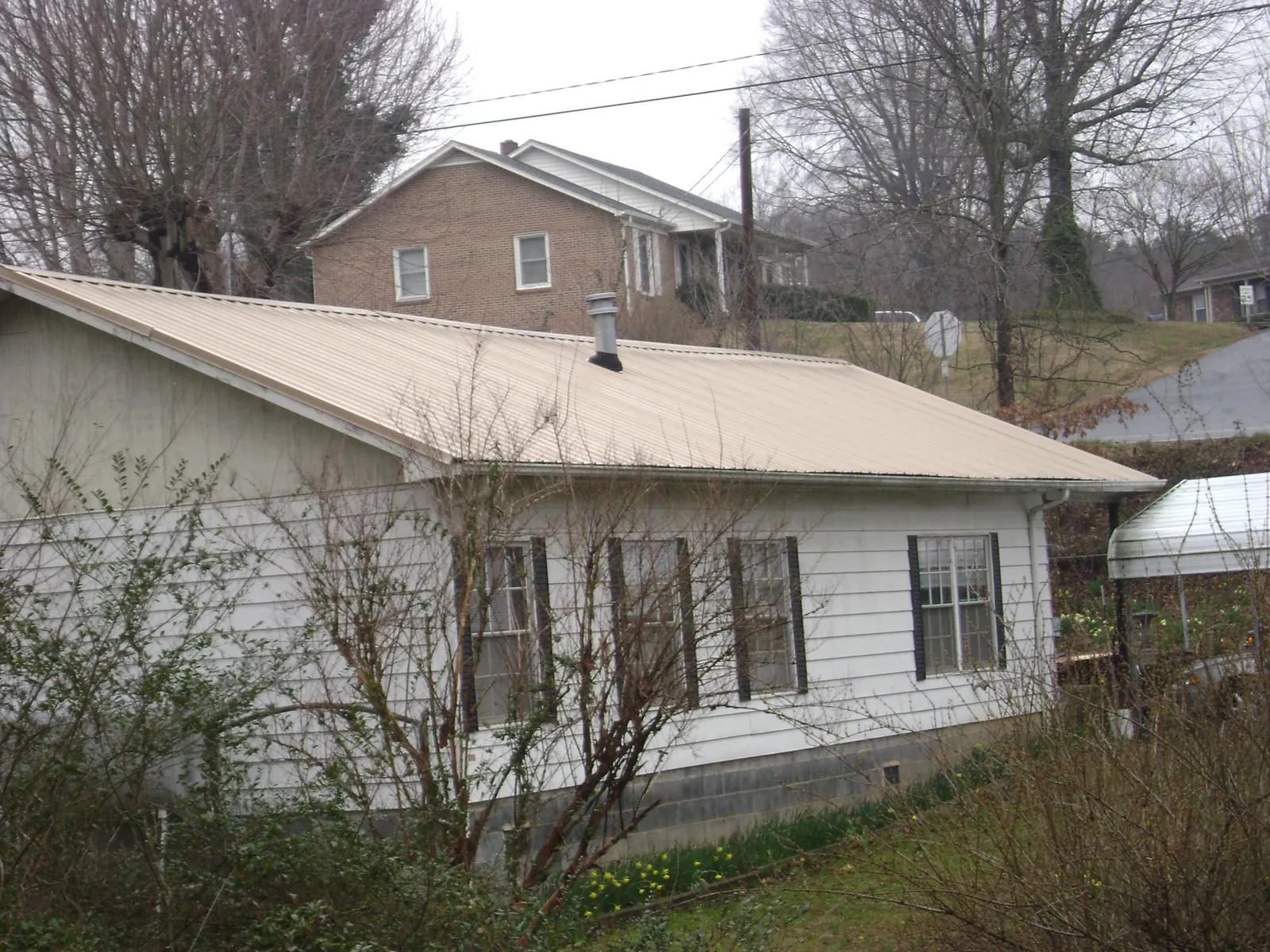 Tan metal roof on a white sided house set into a hillside — Commercial Roofing by Roofing Brothers in Fort Walton Beach