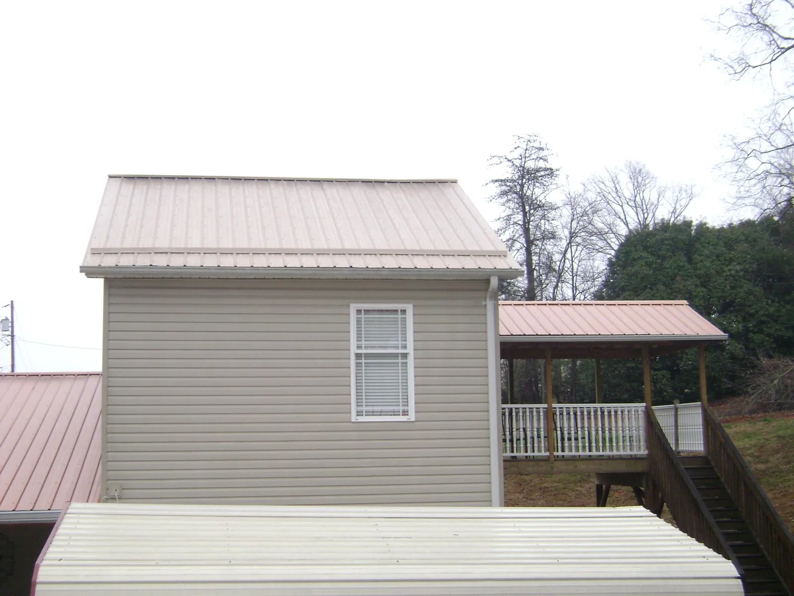 Tan metal roofs on a two story addition and attached porch, from a Roof Replacement job in Fort Walton Beach